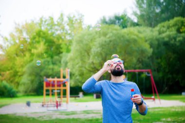 Adam yazın parkta sabun köpüğü üflüyor. Hayatın ve havanın tadını çıkarıyor.