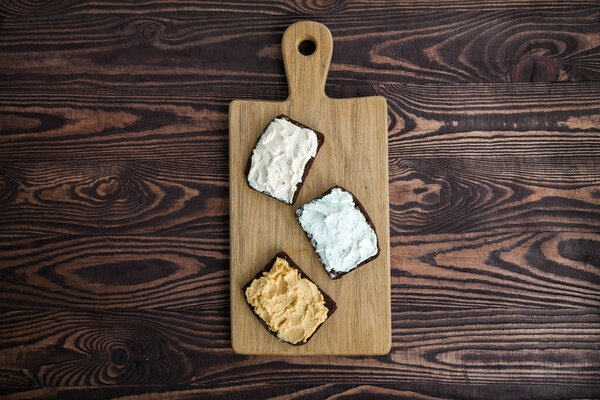 Vegetarian rye bread toasts with cottage cheese and hummus. Wooden board on a rural background, top view, copy-space