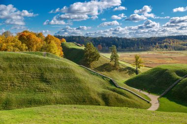 Kernave tepeleri, Litvanya, sonbaharda ince altın renkler ve solgun çayırlarda sallanan bir yol serpilmiş bulutlarla dolu sakin bir gökyüzünün altında