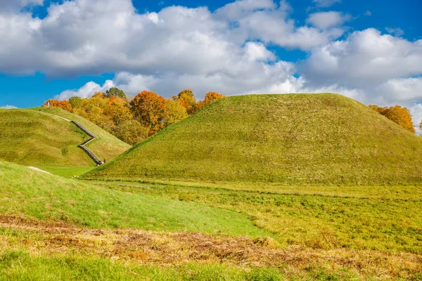 Litvanya 'daki Kernave tepelerinin sonbahar manzarası, bir UNESCO Dünya Mirası sahası, canlı yeşillikler, çimenli yamaçlar ve açık bir gökyüzü altında kültürel manzaralar