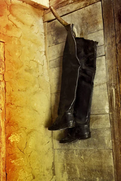 Bir köy kulübe bir kırık sarı duvarda asılı yüksek siyah domuz derisi çizmeler