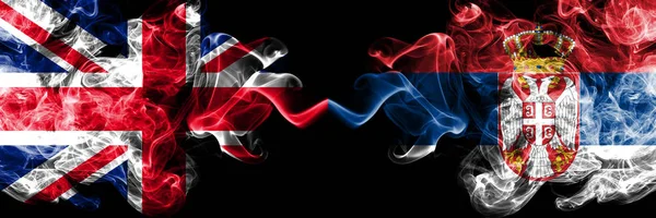 Великобритания против Сербии, сербские дымовые мистические флаги, расставленные бок о бок. Толстые шёлковые дымовые флаги Великобритании и Сербии . — стоковое фото