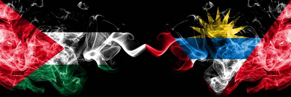 Palestine vs Antigua and Barbuda smoky mystic flags placed side by side. Thick colored silky smokes flag of Palestinians and Antigua and Barbuda