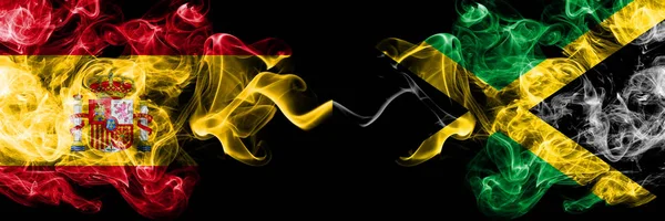 Spania mot Jamaica, jamaicansk røyklignende mystiske flagg plassert side ved side. Tykk, farget, silkeaktig røyk, spansk og jamaicansk flagg, jamaicansk – stockfoto