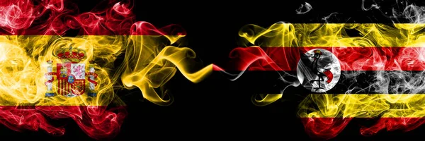 España vs Uganda, banderas místicas humeantes ugandesas colocadas lado a lado. Bandera de humo sedoso de color grueso de España y Uganda, Uganda — Foto de Stock