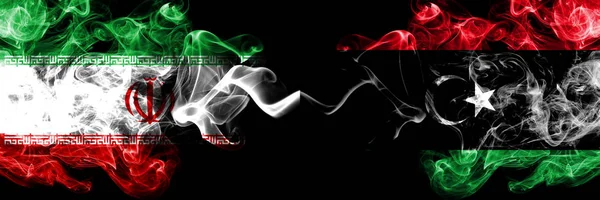 Iran vs Libia, bandiere di stati mistici fumosi libici affiancate. Seta colorata spessa fuma combinazione bandiera di Iran e Libia, libico — Foto Stock