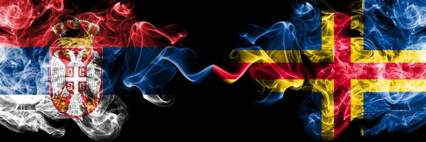 Serbien vs Åland rökig Mystic flaggor placerade sida vid sida. Tjocka färgade silkeslena röker kombination av serbiska och Åland flagga — Stockfoto