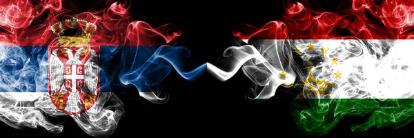 Serbia vs Tayikistán, Banderas místicas humeantes de Tayikistán colocadas una al lado de la otra. Combinación de humo sedoso de color grueso de Serbia y Tayikistán, bandera de Tayikistán — Foto de Stock