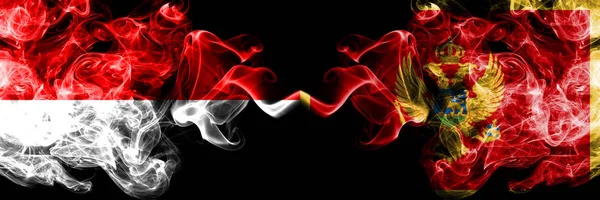 Индонезия - Черногория, Черногория - курящие мистические флаги, расположенные бок о бок. Толстые шёлковые дымовые флаги Индонезии и Черногории — стоковое фото