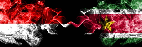 Индонезия против Суринама, суринамские дымящиеся мистические флаги, размещенные бок о бок. Толстые цветные флаги Индонезии и Суринама, Суринама — стоковое фото