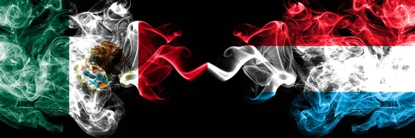 Meksika vs Lüksemburg dumanlı mistik bayraklar yan yana yerleştirilir. Kalın renkli ipeksi soyut Meksika ve Lüksemburg afiş dumanlar
