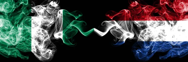 Nigeria vs Países Bajos, banderas místicas ahumadas abstractas holandesas colocadas una al lado de la otra. Banderas de humo sedoso de color grueso de Nigeria y Países Bajos, holandés — Foto de Stock