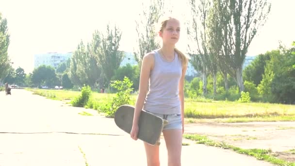 Девочка-подросток идет со скейтбордом под солнцем в замедленной съемке — стоковое видео
