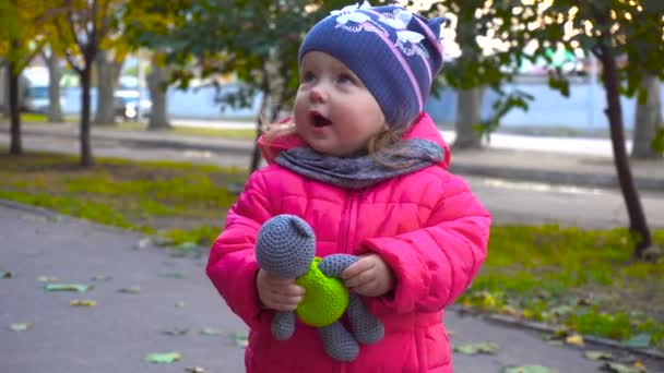 Adorable baby girl holding toy in autumn city — Stock Video