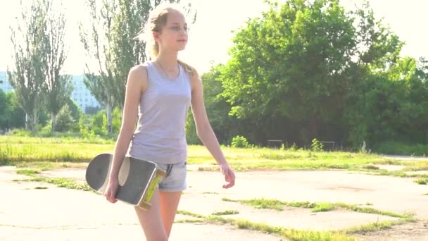 Adolescente marche avec planche à roulettes en plein soleil — Video