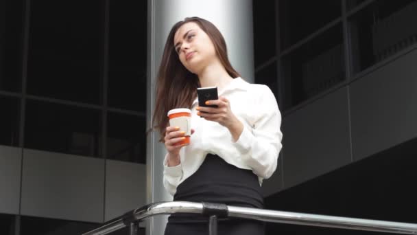 Empresária com bebida quente usando smartphone com escritório atrás — Vídeo de Stock