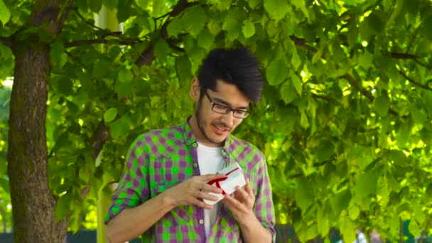 Feliz asiático hombre apertura regalo en parque — Vídeo de stock