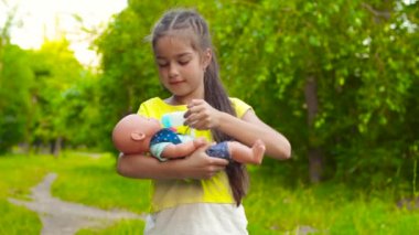 Kız yaz parkta oyuncak bebek besleme