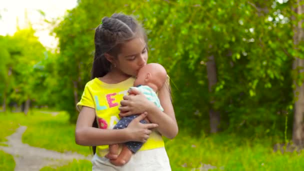 Mädchen füttert und küsst Babypuppe im Park — Stockvideo