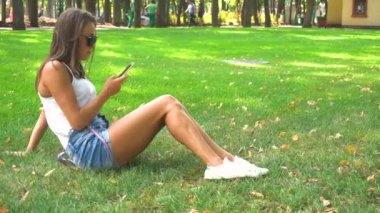 Parkta çim üzerinde akıllı telefon kullanan kadın