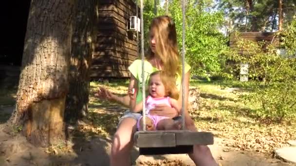 Woman with girl on wooden seesaw under tree — Stock Video