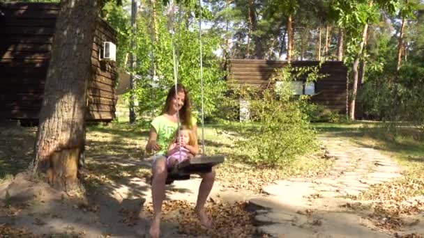 妇女妈妈与女孩在木制摇摆机在树之下 — 图库视频影像