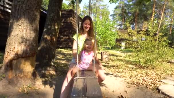 Mother with girl on wooden swing under tree — Stock Video