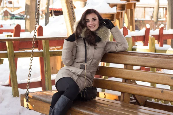 Молодая женщина в зимнем парке сидит на скамейке — стоковое фото