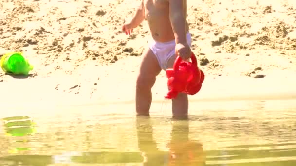 Niña en la playa jugando con la olla de riego — Vídeos de Stock