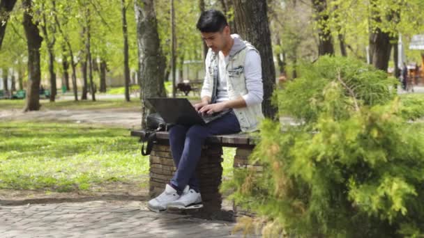 Азіатських людині, сидячи в парку і працюють на ноутбук — стокове відео