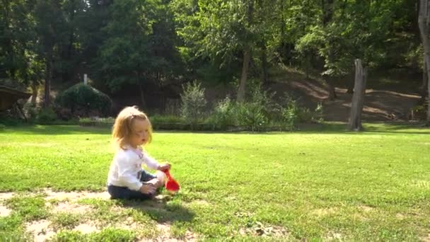 Çimenlerin üzerinde oturan oyuncaklarla oynayan kız — Stok video