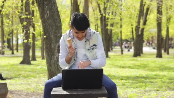 Счастливый человек фрилансер работает на ноутбуке и ест мороженое — стоковое видео