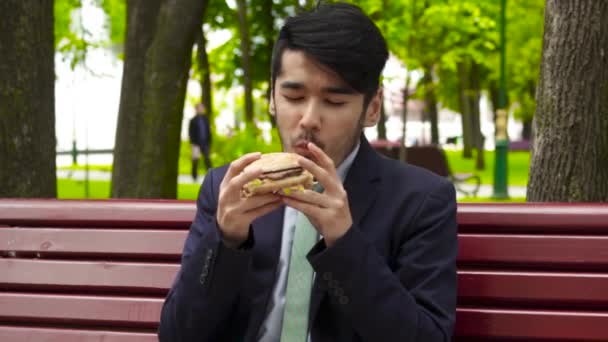 Бізнесмен їсть смачний бургер в парку — стокове відео