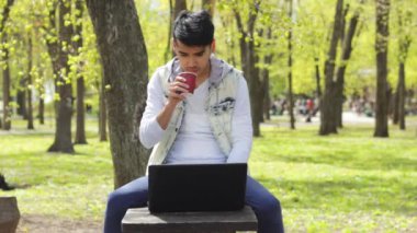 Adam parkta dizüstü bilgisayar üzerinde çalışan kahve ile