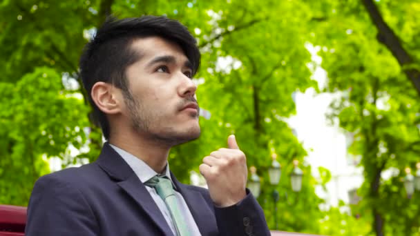 Asiático hombre de negocios sentado en parque y comer francés freír — Vídeo de stock