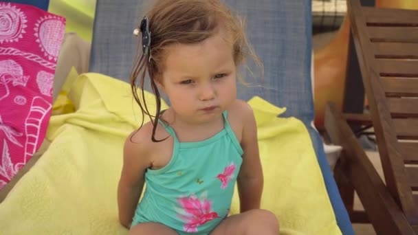 Маленькая девочка сидит на шезлонге и ест что-нибудь перекусить — стоковое видео