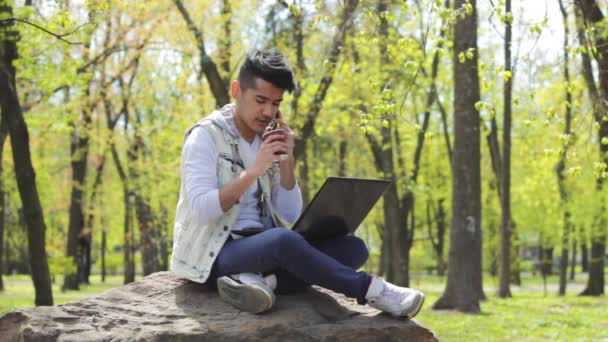 Student Azjatycki Człowiek Rozmawia Przez Telefon Siedzi Parku Laptopem Kolanach — Wideo stockowe