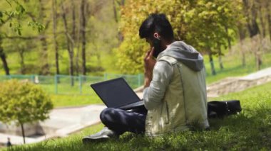 Parkta oturan telefonla konuşan programcı adam
