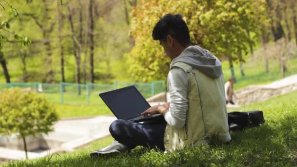 坐在草地上的人程序员在公园里的笔记本电脑上工作 — 图库视频影像
