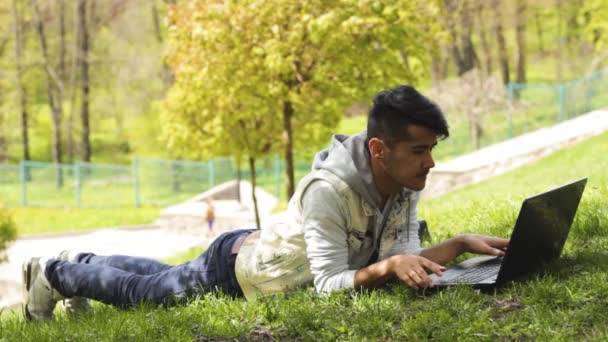 Hombre freelancer trabajando en el ordenador portátil y acostado en la hierba — Vídeos de Stock