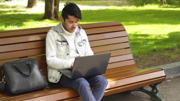 Uomo che lavora su un computer portatile seduto nel parco — Video Stock