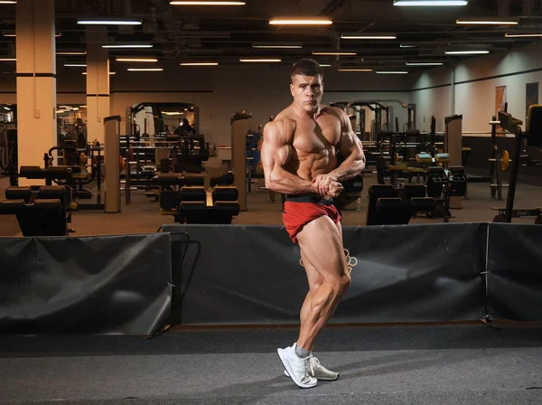 Hombre joven culturista de pie en el gimnasio y posando —  Fotos de Stock