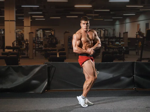 Spor salonunda duran ve poz genç adam vücut geliştiricisi. Çok iyi bodyshape.