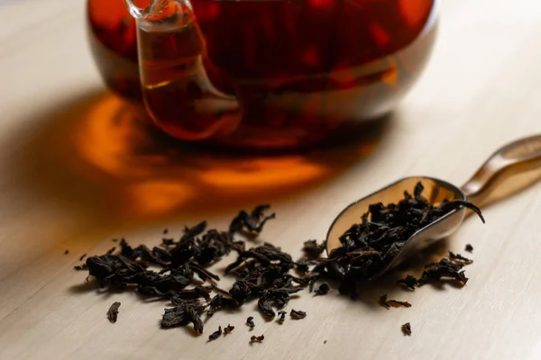 Black tea leafs on the wooden table and teapot — Stock Photo, Image