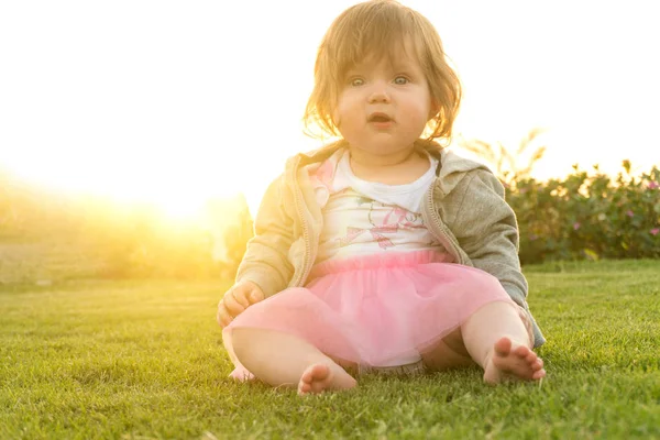 Grappig meisje zittend op gras op zonsondergang — Stockfoto