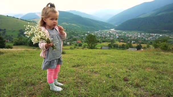 Κορίτσι παιδί στέκεται με λουλούδια και τρώει μερικά σνακ — Αρχείο Βίντεο