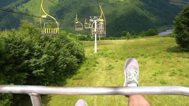 El hombre sentado en el telesilla y sus pies tiemblan sobre la montaña — Vídeo de stock