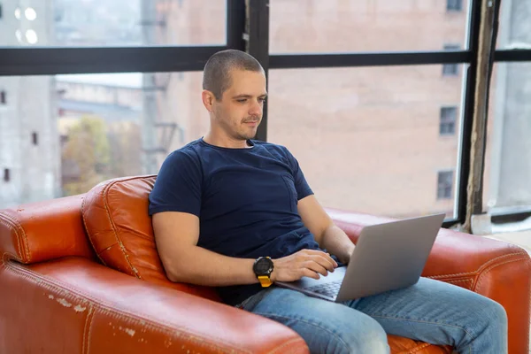 Homme assis dans un fauteuil rouge ancien style et travaillant sur un ordinateur portable. — Photo