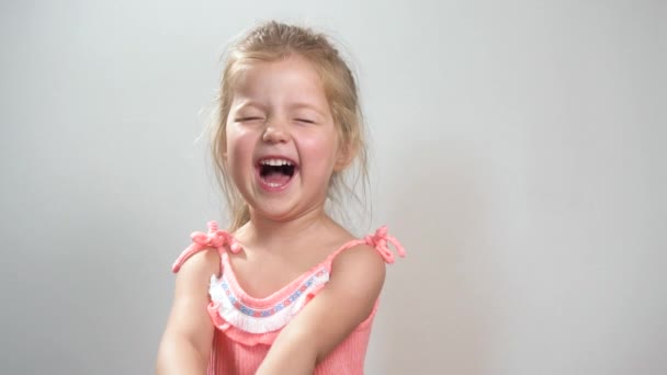 Смеющаяся маленькая девочка в розовом платье смотрит в камеру дома — стоковое видео