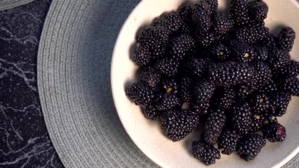 Hand of child taking blackberry from bowl with berries on the table. — Stock Video